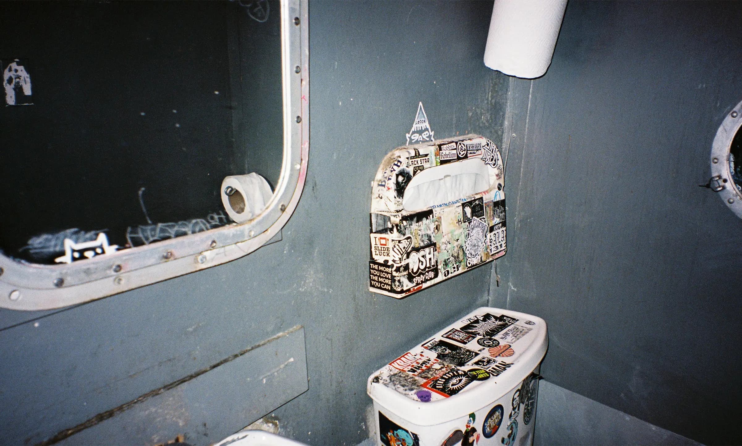 A grungy, sticker-covered venue bathroom shot on film